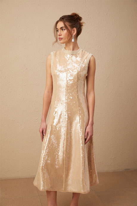 A woman wearing a shimmering midi dress adorned with faux pearls and sequins posing elegantly against a plain background