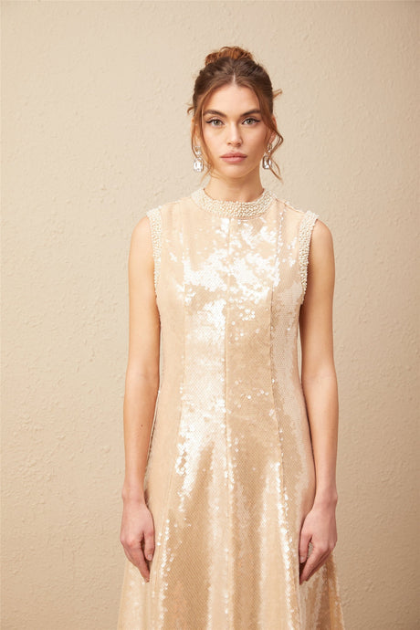 A woman wearing a shimmering midi dress adorned with faux pearls and sequins posing elegantly against a plain background