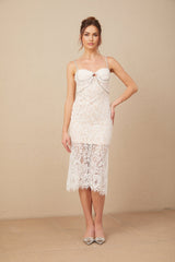 A woman wearing a sleek white lace midi dress with a crystal embellished bustier top and delicate spaghetti straps