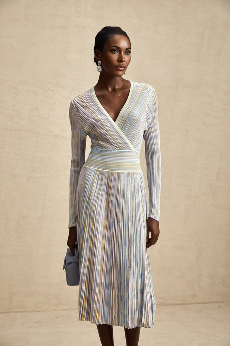 A woman wearing a vertical striped knitted midi dress with long sleeves in multiple colors standing against a plain background