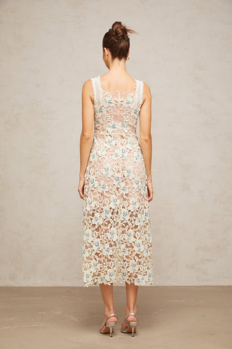 A woman wearing a white Aline midi dress with floral lace detailing standing against a plain background