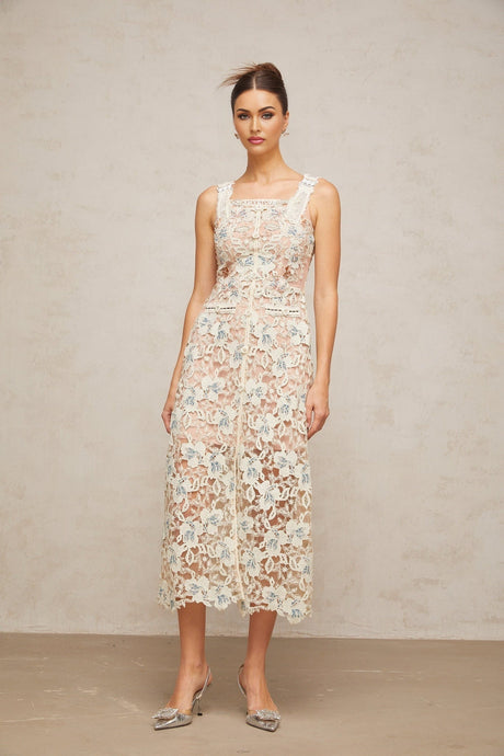 A woman wearing a white Aline midi dress with floral lace detailing standing in a neutral background