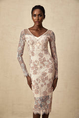 A woman wearing a white fitted midi dress with intricate guipure lace pattern standing against a plain background