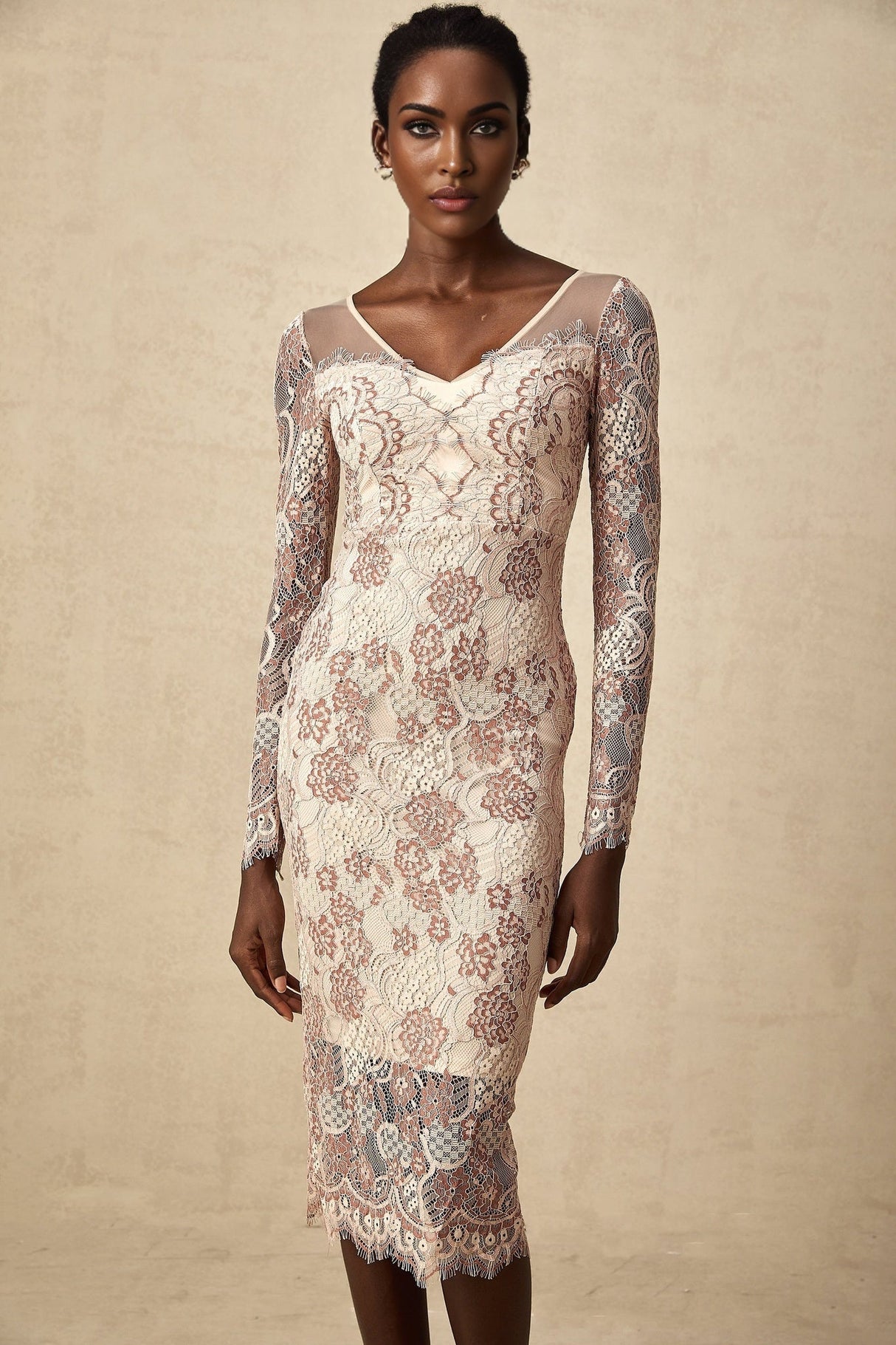 A woman wearing a white formfitting midi dress with intricate guipure lace patterns standing against a plain background