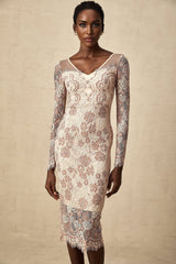 A woman wearing a white formfitting midi dress with intricate guipure lace patterns standing against a plain background