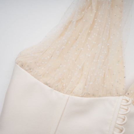 A woman wearing a white halterneck tulle midi dress with a fitted bodice and flowing skirt standing against a plain background