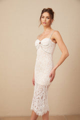 A woman wearing a white lace midi dress with a crystal embellished bustier top and delicate floral lace pattern throughout the bodice and skirt