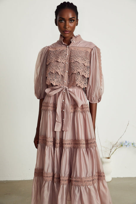 A woman wearing a white lace midi dress with tiered skirt and cut out details standing in a neutral backdrop