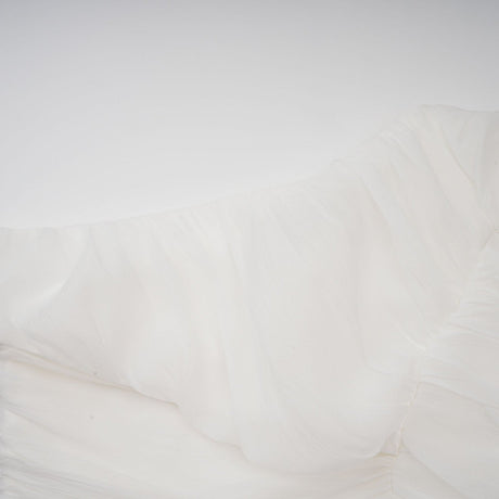 A woman wearing a white matching set consisting of a creased top and trousers standing against a plain background