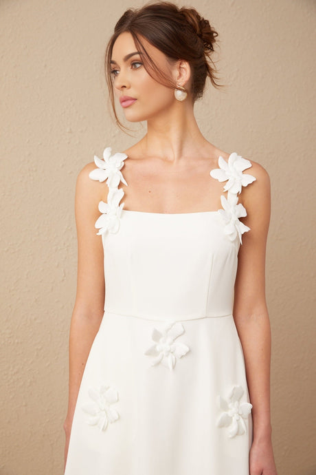 A woman wearing a white midi dress with a square neckline and faux flower embellishments standing in a neutral pose