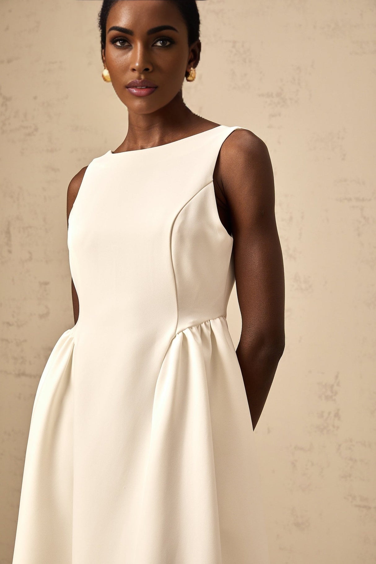 A woman wearing a white sleeveless midi dress with a full skirt standing against a plain background