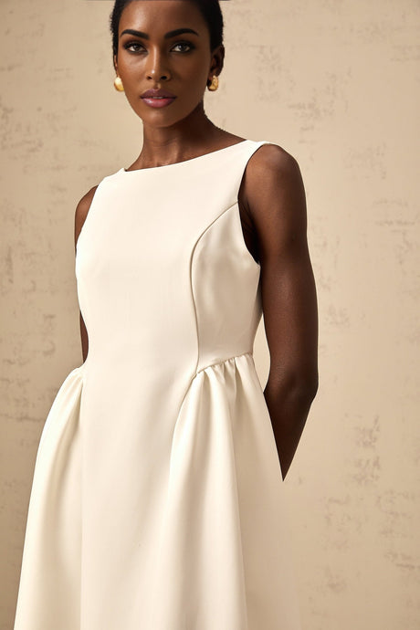 A woman wearing a white sleeveless midi dress with a full skirt standing against a plain background