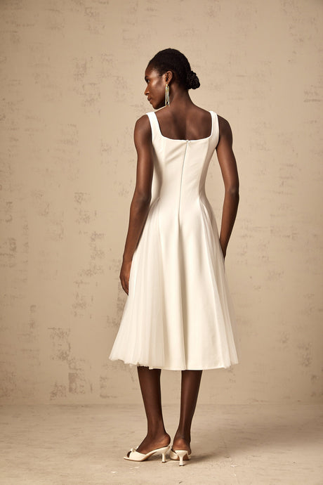 A woman wearing a white tulle midi dress with godet inserts standing against a plain background