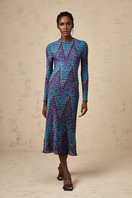 A woman wearing a zigzag patterned knitted midi dress with long sleeves standing against a plain background