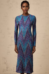 A woman wearing a zigzag patterned knitted midi dress with long sleeves standing against a plain background