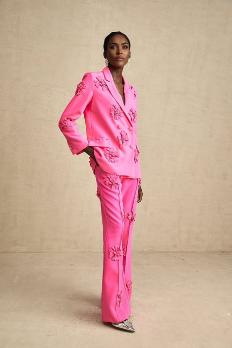 A young girl wearing a pink floral jacket and matching trousers standing against a plain background