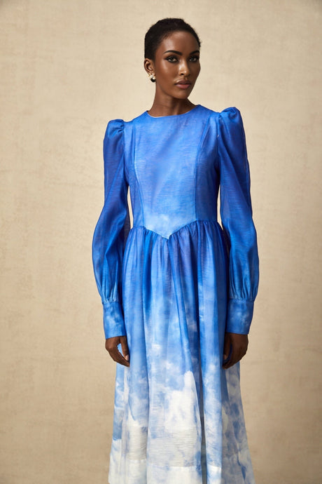 Woman wearing a blue gradient pleated midi dress with a flowing silhouette and elegant drape