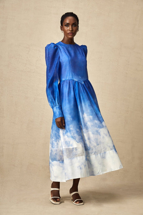 Woman wearing a blue gradient pleated midi dress with a flowing skirt and sleeveless design against a plain background