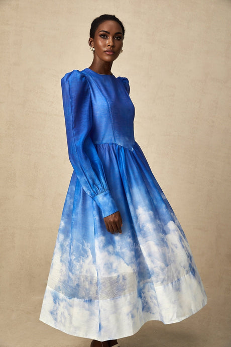 Woman wearing a blue gradient pleated midi dress with a flowy silhouette and varying shades of blue from light to dark