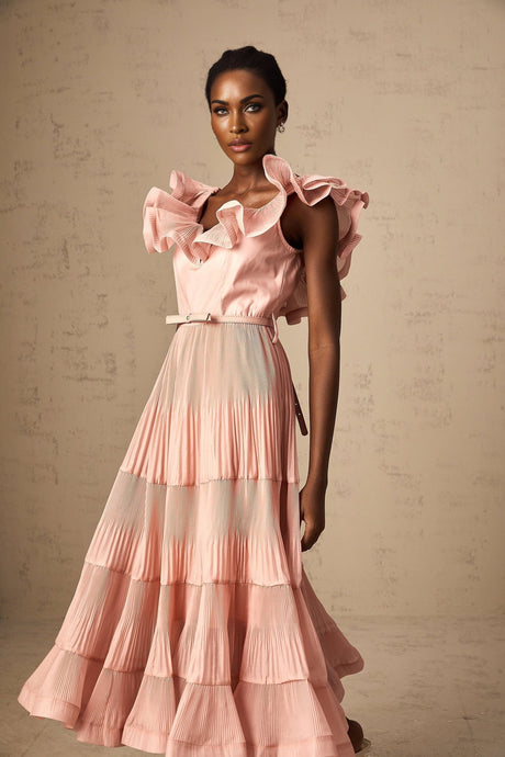 Woman wearing a coralpink midi dress with pleated details and frilly accents standing against a plain background
