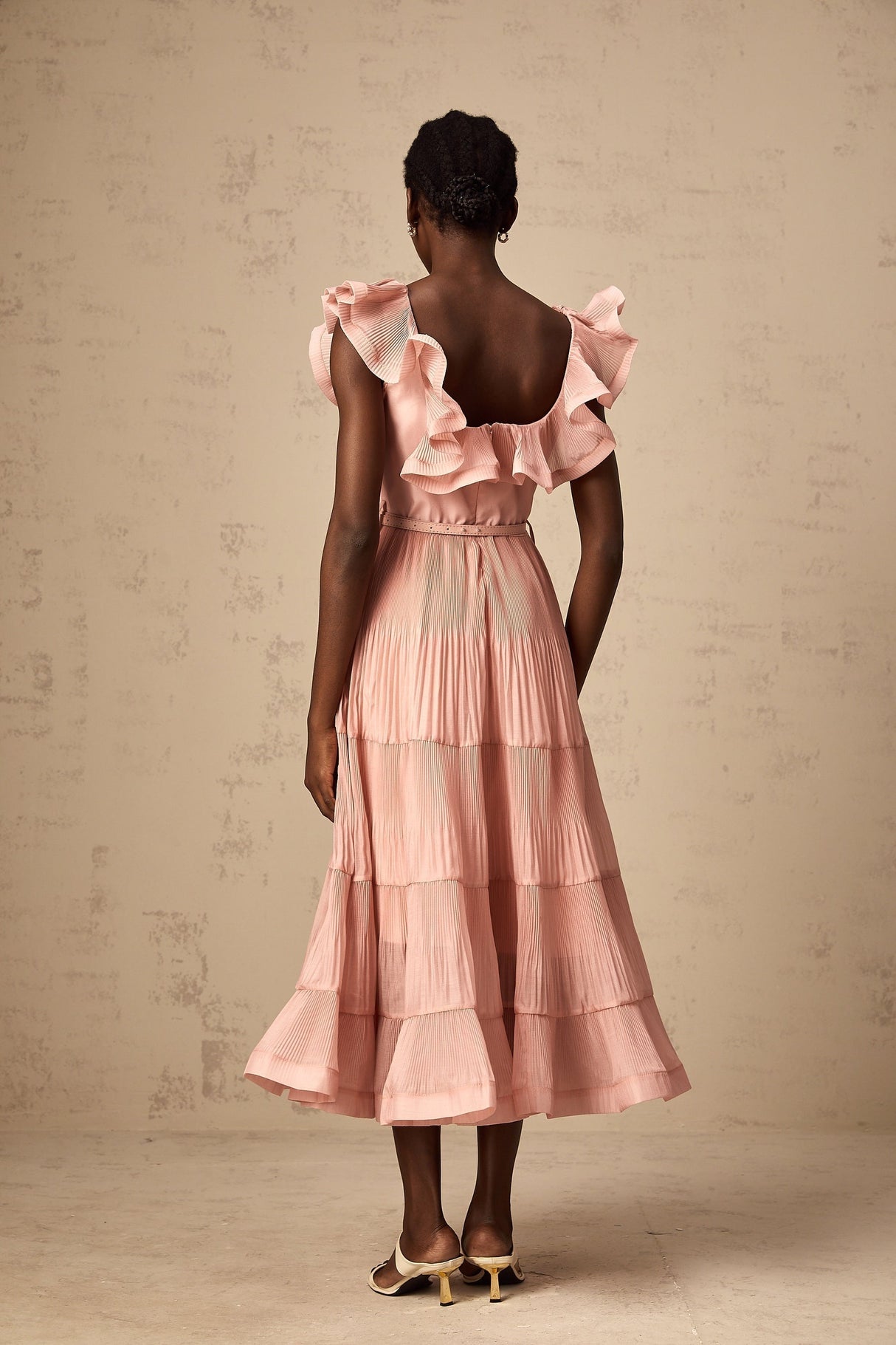 Woman wearing a coralpink midi dress with pleated frills and a flowy silhouette