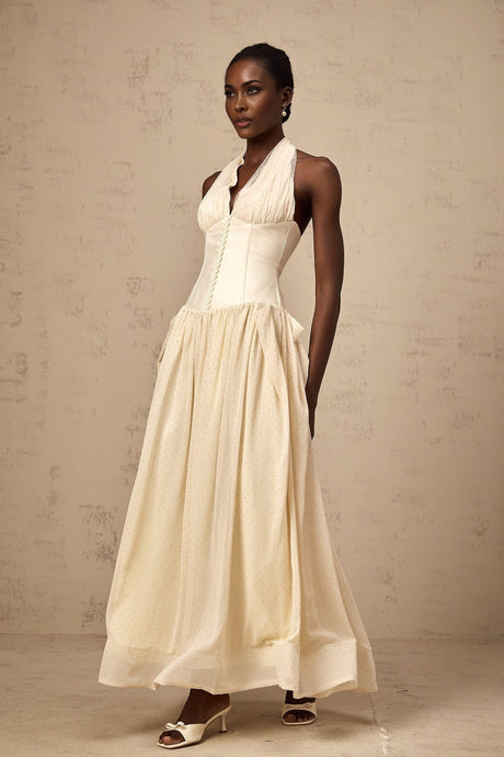 Woman wearing a halterneck tulle midi dress in pale pink with a fitted bodice and flowy skirt standing against a plain background