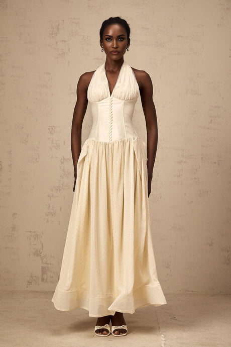 Woman wearing a light colored halterneck tulle midi dress with a flared skirt standing in a neutral background