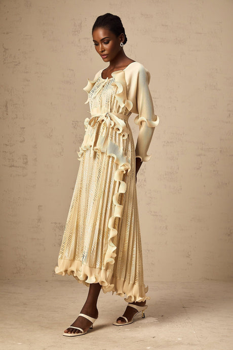 Woman wearing a neutral colored ruffled midi dress with gilded accents standing in a relaxed pose