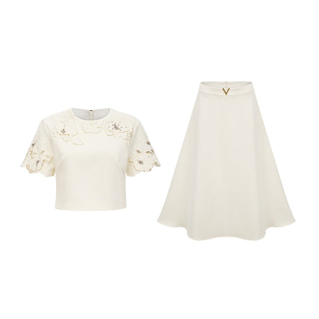 Woman wearing a neutral colored twopiece outfit with a sleeveless top and skirt featuring threedimensional petal details