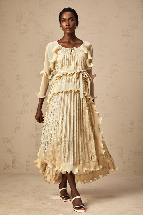Woman wearing a neutral tone midi dress with ruffled details and gilded accents standing in a casual pose