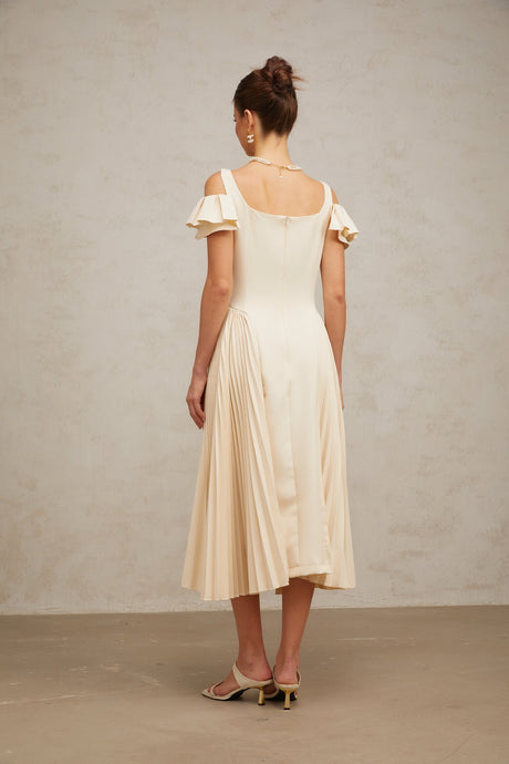 Woman wearing a neutralcolored pleated midi dress with a flared skirt and fitted bodice standing in a relaxed pose