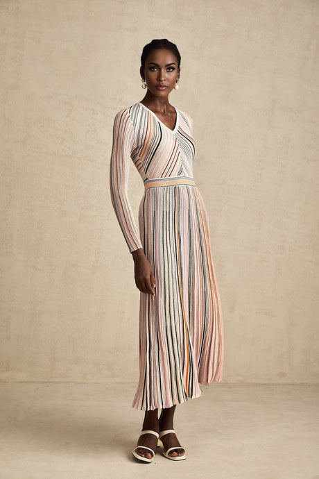 Woman wearing a pink metallic pleated midi dress with a flowing skirt and fitted bodice standing against a plain background