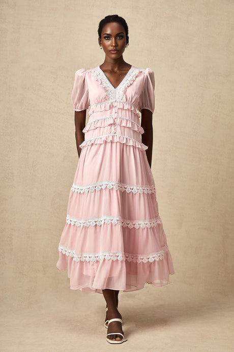 Woman wearing a pink midi dress with ruffled tiers and sleeveless design standing against a plain background