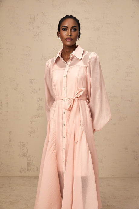 Woman wearing a pink midi length shirt dress with tied waist detail and button front closure