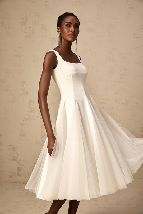 Woman wearing a white tulle midi dress with godet inserts and flared skirt standing in a neutral background
