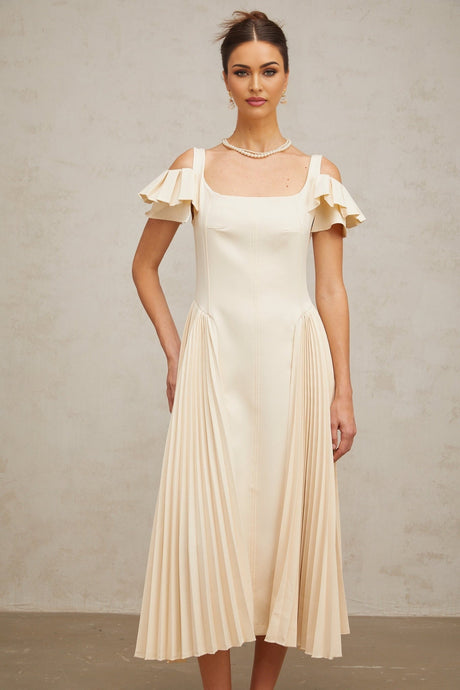 Woman wearing beige pleated midi dress with flared skirt and neutral tones standing in elegant pose
