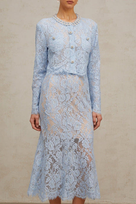 Woman wearing blue floral lace crop top and matching skirt set against plain background