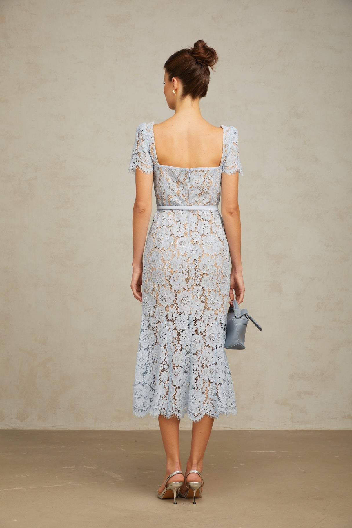 Woman wearing blue floral lace midi dress with boned bodice and fitted silhouette standing against plain background