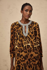 Woman wearing brown leopard print midi dress with embellishments and long sleeves standing against plain background