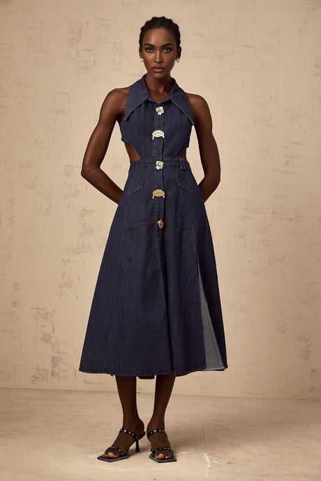 Woman wearing dark blue denim midi dress with cut out details on sides standing against plain background