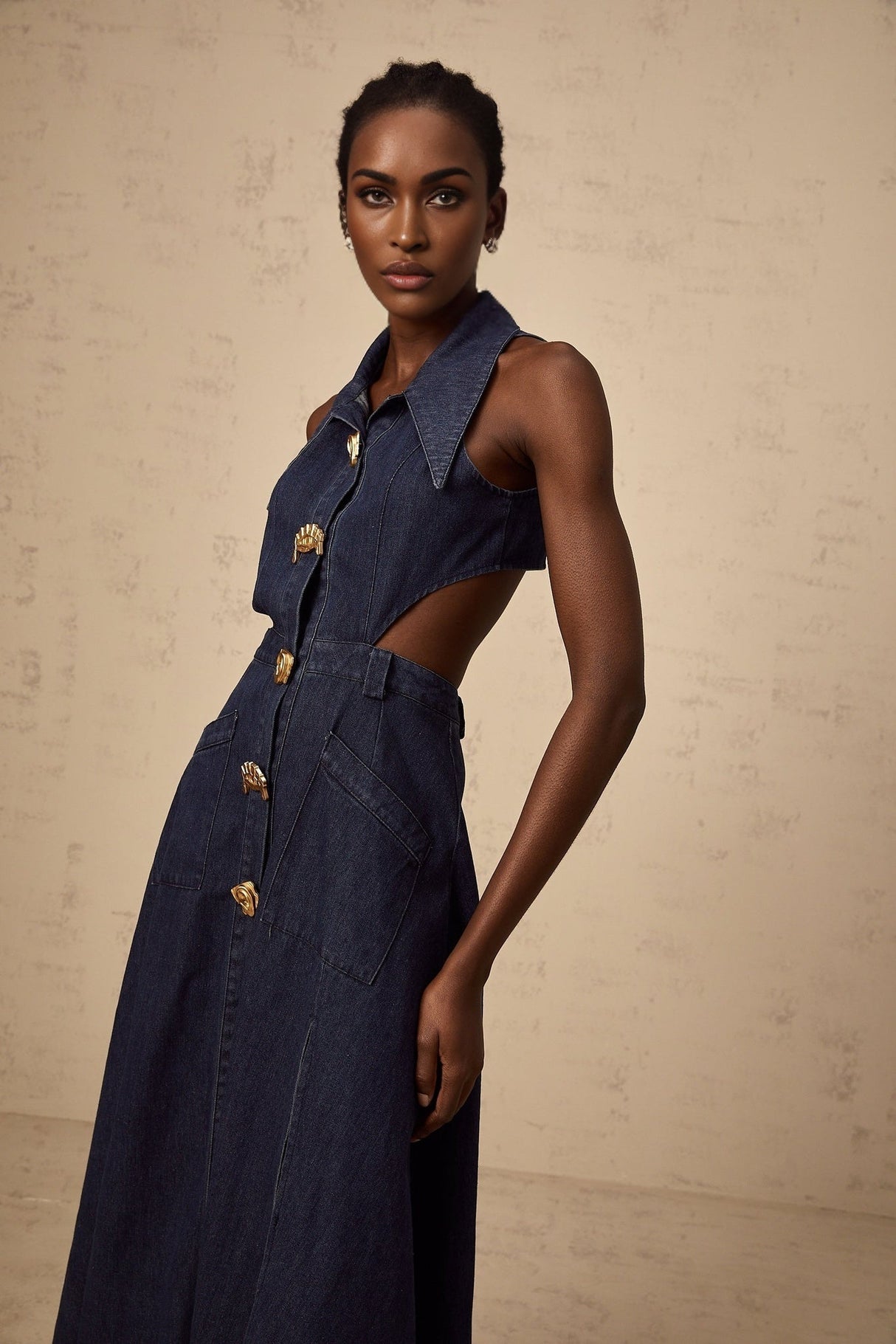 Woman wearing dark blue denim midi dress with cutout details standing against plain background
