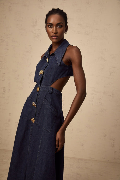 Woman wearing dark blue denim midi dress with cutout details standing against plain background