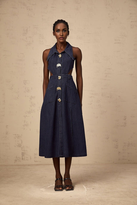 Woman wearing dark blue denim midi dress with cutout details standing against plain background