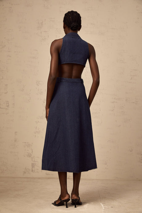 Woman wearing dark blue denim midi dress with cutout details standing against plain background