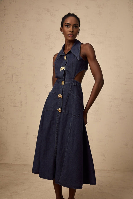 Woman wearing dark blue denim midi dress with cutout details standing against plain background