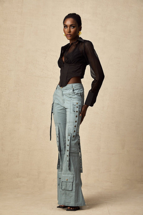 Woman wearing green flared cargo trousers with belt loops and multiple pockets standing against white background