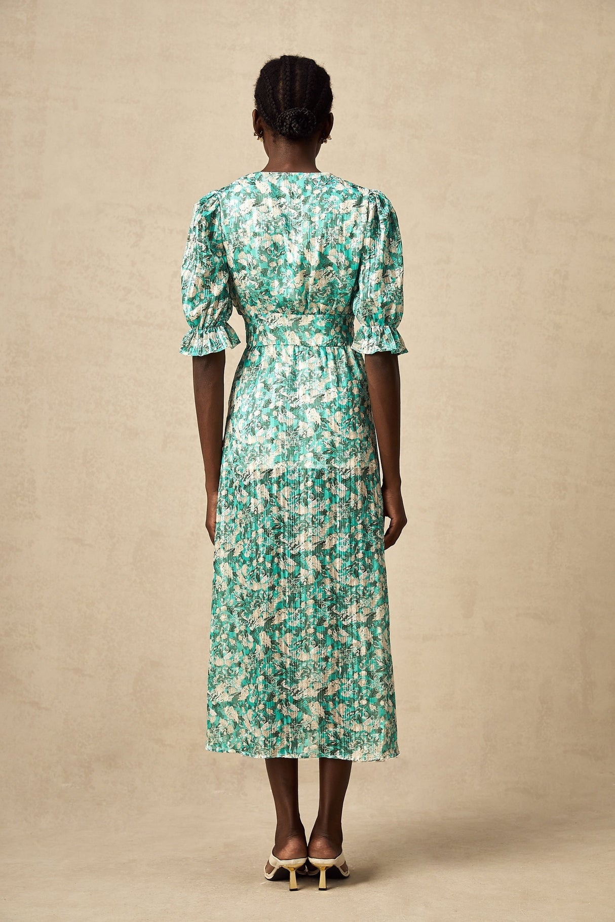 Woman wearing green floral print midi dress with high slit standing against plain background