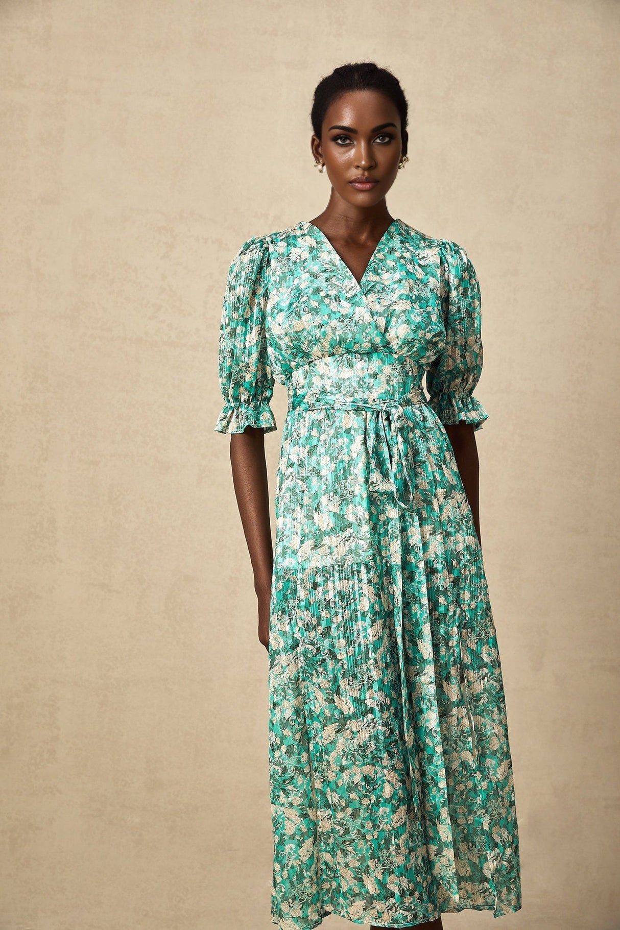 Woman wearing green midi dress with floral print and high slit standing against plain background