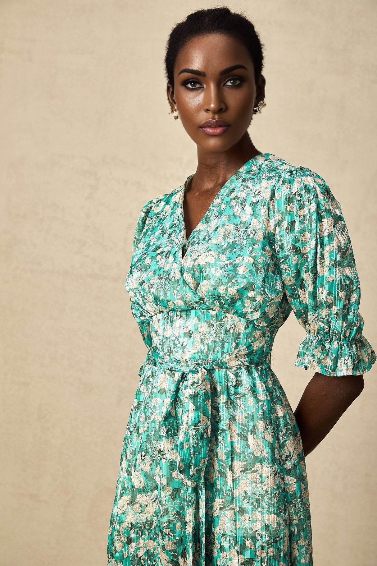 Woman wearing green midi dress with floral print and high slit standing against plain background