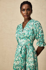 Woman wearing green midi dress with floral print and high slit standing against plain background